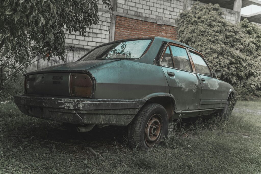 A rusted, old car sits abandoned amidst overgrown grass, embodying decay and nostalgia.